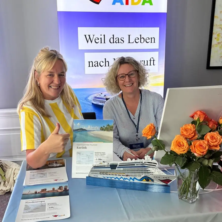 Zwei Kolleginnen beraten am AIDA-Tisch mit Schiffsmodell und Reiseflyern